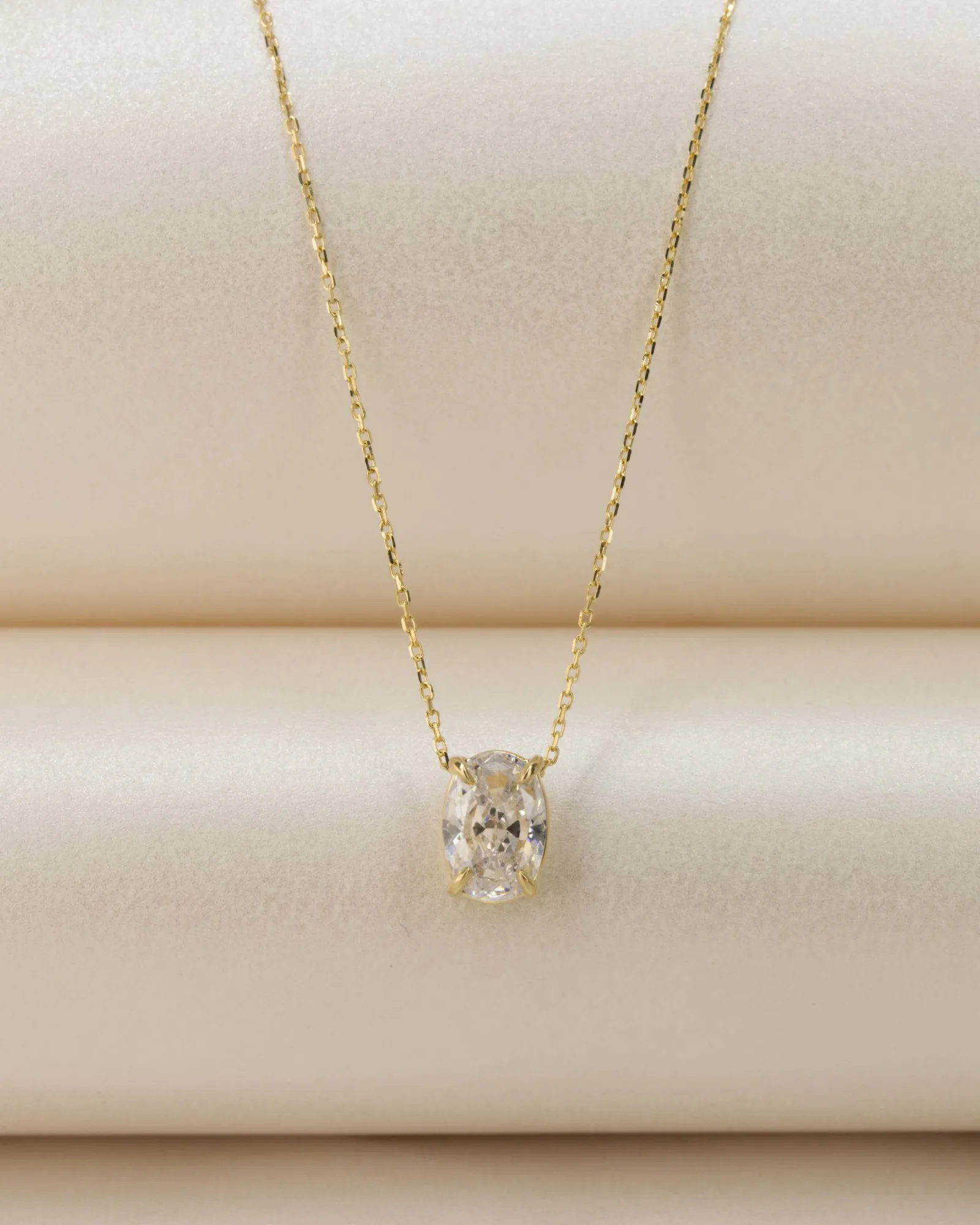 Oval diamond pendant on a fine gold chain, resting on champagne silk